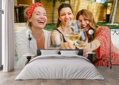 Three adult beautiful caucasian women female friends sitting outdoor in backyard with glasses of white wine having fun celebrating and drinking in summer day on vacation holiday - real people leisure Wall mural