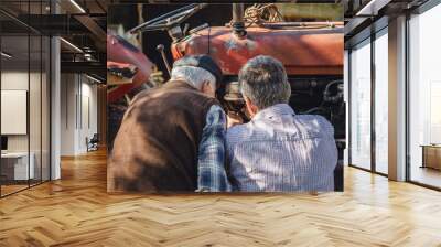 Two caucasian senior men father and son pensioner at the farm repairing the tractor machine in sunny day family bonding generation cooperation and togetherness concept real people Wall mural