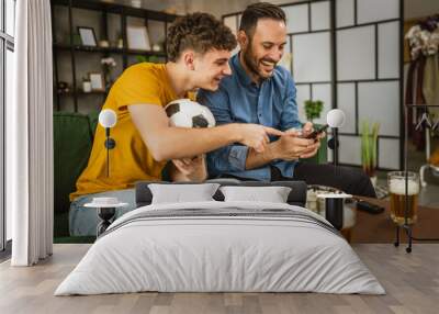 Two male friends follow football match results on mobile phone at home Wall mural