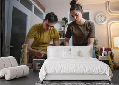 Two people young adult couple man and woman husband and wife or boyfriend and girlfriend preparing pizza food at home helping each other cutting and add ingredients and spices real people copy space Wall mural