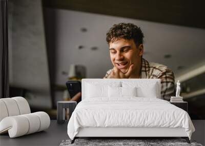 young adult caucasian boy sit indoor and use mobile phone Wall mural