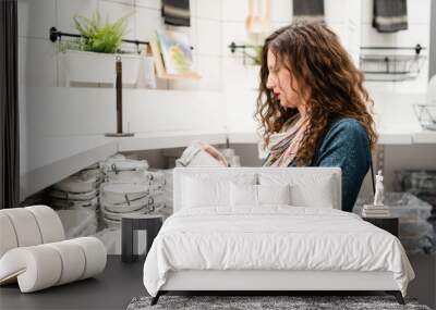 Young caucasian woman with curly black hair at the shopping mall store looking to the bowl product price by the white shelf alone side view Wall mural