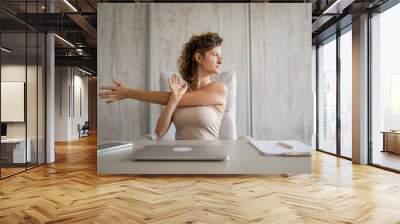 young woman stretching at work while sitting at desk having back pain Wall mural