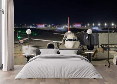 an airplane stands on the boarding bridge at night with a moving plane in the background Wall mural