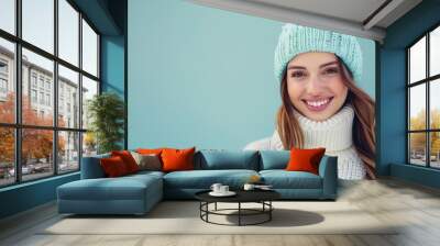 Joyful happy woman in blue winter hat and white sweater posing against blue studio wall background, beauty fashion portrait Wall mural