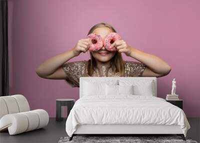 Beautiful young girl holding two donut on pink wall background. Child having fun with doughnut. Happy birthday party, celebration and holiday concept Wall mural