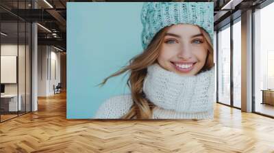 Charming happy woman in blue winter hat and white sweater posing against blue studio wall background, beauty fashion portrait Wall mural