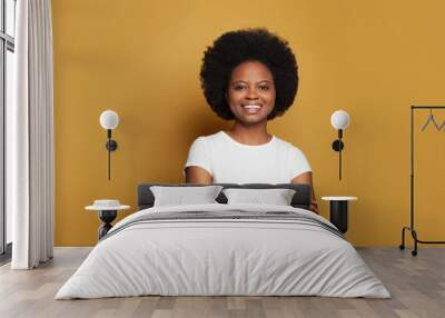 Cute attractive young woman in empty white t-shirt standing with crossed arms and smiling on bright yellow background Wall mural