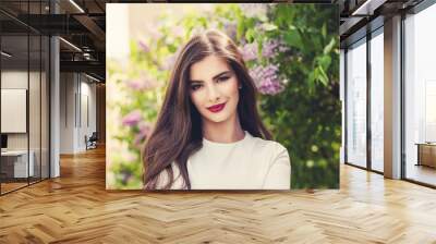 Healthy smiling woman with long hair and makeup on lilac flowers background outdoors Wall mural