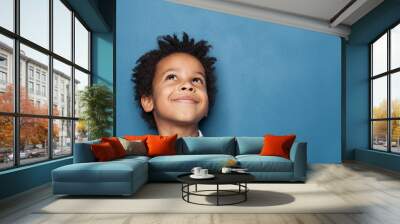 Little black child boy smiling and looking up on blue background Wall mural