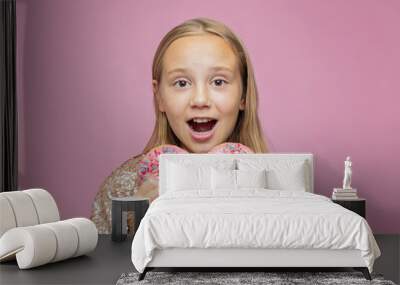 Little happy surprised cute girl is eating donut on pink wall background. Child is having fun with doughnut. Tasty food for kid. Funny time with sweet food Wall mural