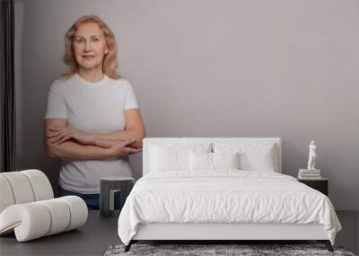 Optimistic confident senior woman wearing white t-shirt standing with crossed arms on gray studio wall background Wall mural