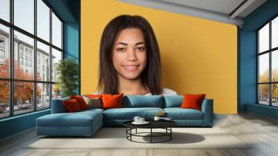 Smiling mixed race young woman in striped shirt on yellow studio background Wall mural