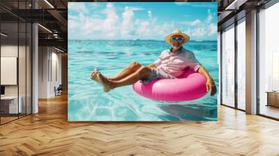 happy old man in summer and hat with sunglasses is sitting on an inflatable pink ring Wall mural