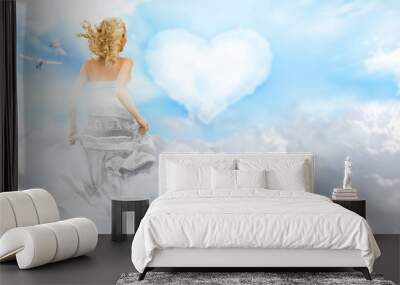 happy young woman running across clouds in the sky. heart on bac Wall mural