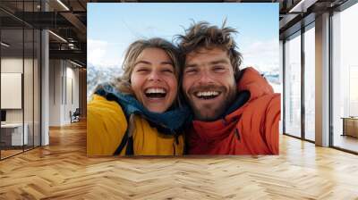 A joyful couple in vibrant ski jackets smiles while enjoying a moment in a picturesque snowy landscape, capturing the essence of adventure, warmth, and togetherness. Wall mural