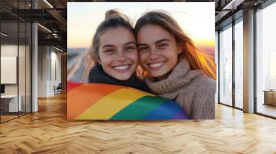 A joyful moment of two women embracing with a rainbow flag, capturing themes of friendship, love, and inclusivity under a golden sunset glow. Wall mural