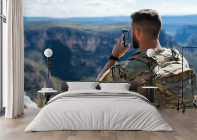 A soldier in tactical camouflage takes a moment to capture the grand canyon view on his phone, marking a moment of tranquility amidst military endeavors. Wall mural