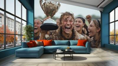 Despite being covered in mud, girls joyfully hold up a trophy after a match, their faces radiating satisfaction and pride, highlighting their determination and team spirit. Wall mural