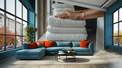 The image shows a person's hands neatly stacking freshly laundered white towels on a wooden shelf, capturing a moment of cleanliness and organization in a home or hotel setting. Wall mural