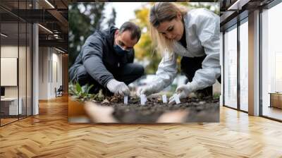 Two forensic experts in protective gear are meticulously marking evidence in a natural setting, highlighting precision and scientific inquiry amidst nature. Wall mural