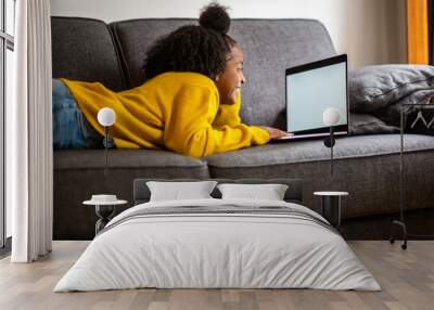 african american girl lying on sofa looking at laptop computer screen at home Wall mural