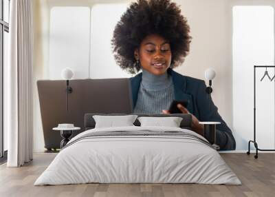 afro american business woman sitting in office working with phone and laptop Wall mural