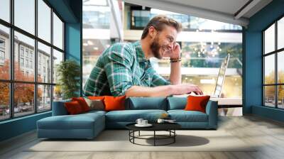 Attractive man smiling with laptop in shopping mall Wall mural