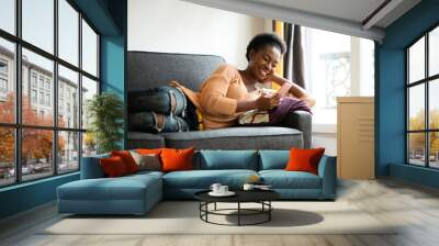 beautiful young black woman relaxing on sofa with mobile phone Wall mural