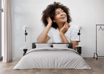 cheerful young african american woman laughing and looking up by white background Wall mural