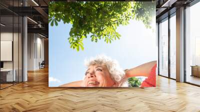 Close up attractive smiling middle aged woman with hands behind head outside in nature Wall mural