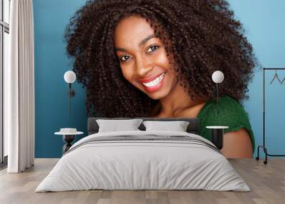 Close up beautiful young african woman with curly hair smiling on blue background Wall mural