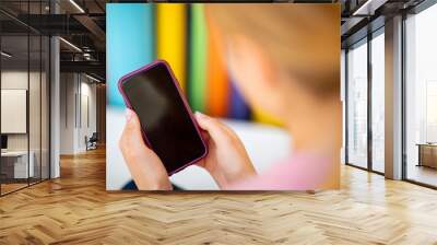 Close up behind of blond girl holding cellphone by colorful background Wall mural