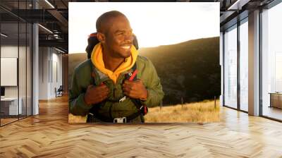 Close up handsome young african american man with backpack smiling with sunset in background Wall mural