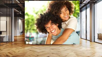 Close up happy afro man giving piggyback to smiling girlfriend outside Wall mural