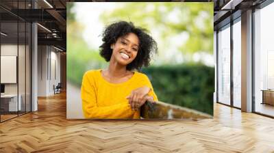 Close up of happy young black woman relaxing on bench outdoors Wall mural