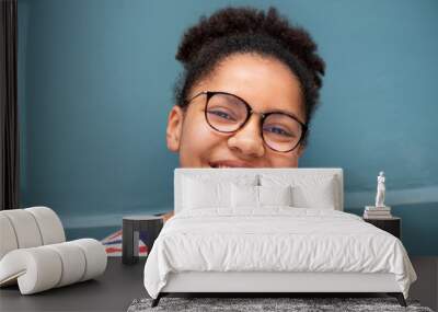 Close up of smiling young mixed race girl with glasses against blue wall Wall mural