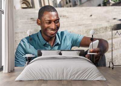 Close up smiling young African american man looking at cellphone outside Wall mural