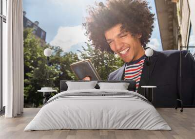 Close up smiling young arab guy with afro hair looking at mobile phone outside Wall mural