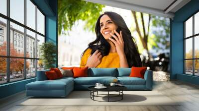 Close up smiling young brunette woman walking and talking with cellphone in city Wall mural