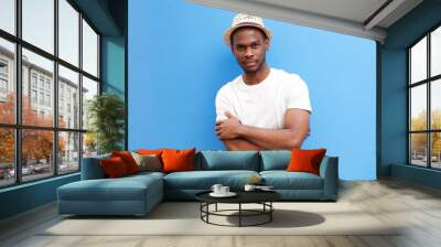 cool young black guy with hat posing with arms crossed against blue background Wall mural