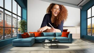 happy female college student sitting at desk writing in book Wall mural