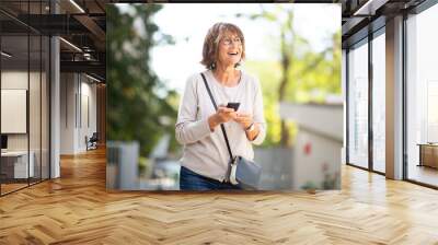 happy older woman laughing with mobile phone outside Wall mural