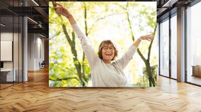 happy older woman with arms outstretched in nature Wall mural