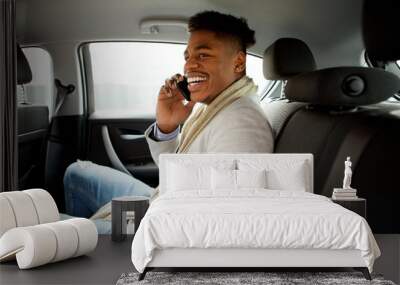 happy young black man sitting in backseat of car and talking with mobile phone Wall mural