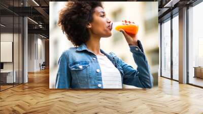 happy young black woman drinking from juice bottle in city Wall mural