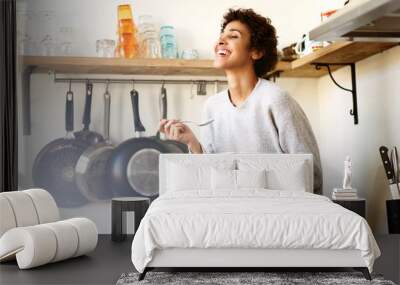 happy young woman eating cereal from bowl in kitchen at home Wall mural