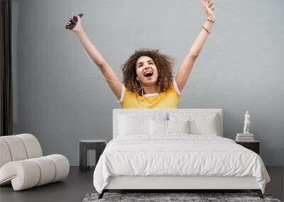 happy young woman with arms raised holding mobile phone and listening to music by gray background Wall mural