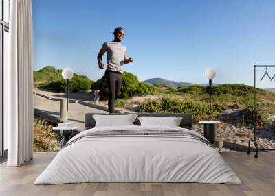 Healthy young african man running on boardwalk at the beach Wall mural