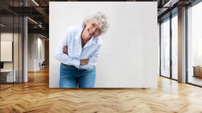 older woman laughing with arms crossed by gray wall Wall mural